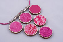 Pink statement necklace made with fabric on light wood base