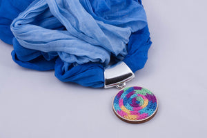 Blue scarf with pendant made with multi-color yarn on light wood base 